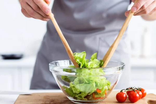 Close-up partial view of man in apron cooking vegetable salad — Stock Photo