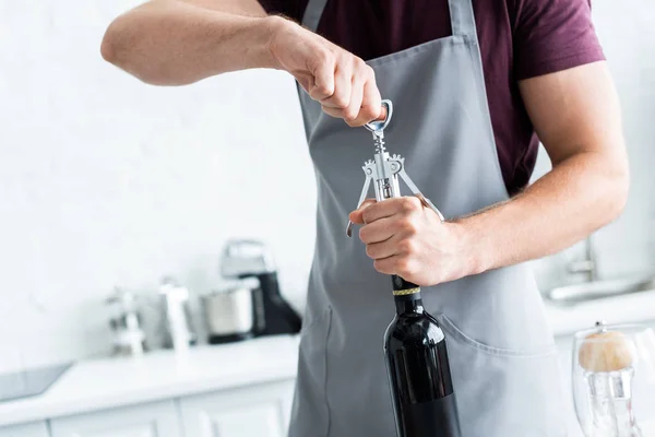 Cropped shot of man in apron opening bottle of wine — Stock Photo