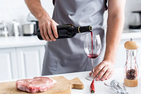 Tiro recortado del hombre en delantal verter vino tinto mientras se cocina filete - foto de stock