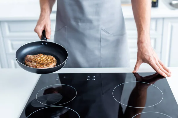 Cropped shot of man in apron holding frying pan with delicious steak — Stock Photo