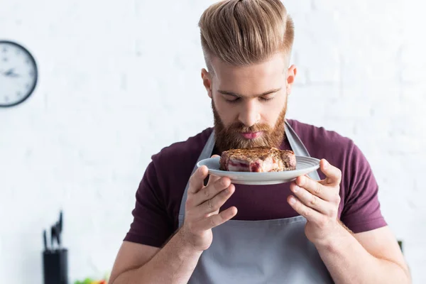 Schöner bärtiger junger Mann in Schürze mit leckerem Rindersteak — Stockfoto