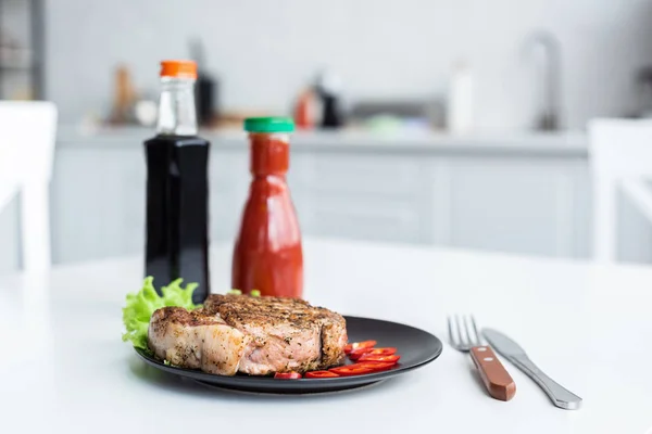 Delicious grilled steak, sauces and fork with knife on table — Stock Photo