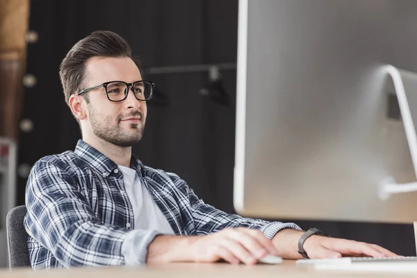 Улыбающийся молодой человек в очках за настольным компьютером на рабочем месте — стоковое фото