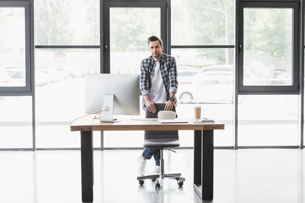 Schöner junger Programmierer, der am Arbeitsplatz in die Kamera schaut — Stockfoto