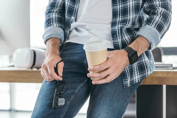 Tiro cortado de homem segurando óculos e café para ir — Fotografia de Stock