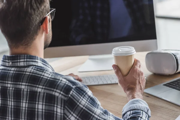 Colpo ritagliato di uomo in occhiali che tengono il caffè per andare e utilizzando il computer desktop — Foto stock