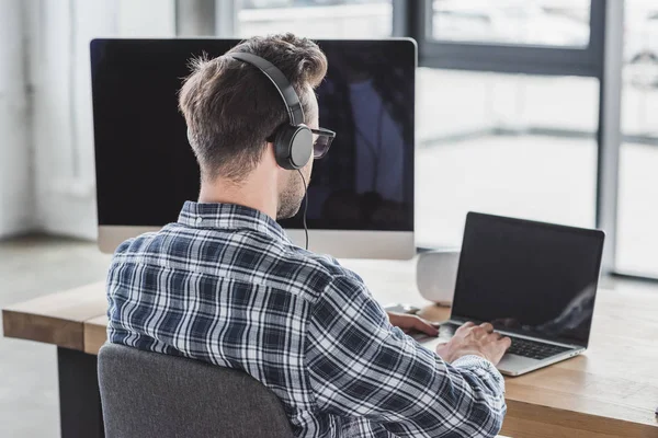 Visão traseira do programador jovem em fones de ouvido e óculos que trabalham com laptop — Fotografia de Stock