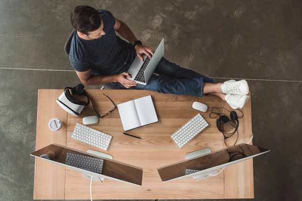 Vista aérea del hombre joven utilizando computadoras portátiles y de escritorio en el lugar de trabajo - foto de stock