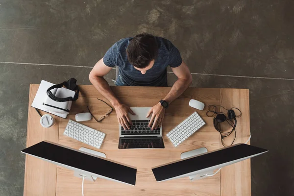 Overhead-Ansicht des jungen Programmierers mit Laptop und Desktop-Computern am Arbeitsplatz — Stockfoto