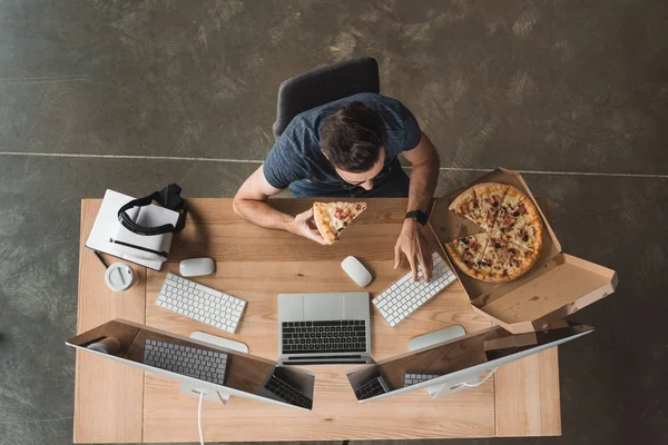 Overhead view of programmer eating pizza and using computers at workplace — Stock Photo