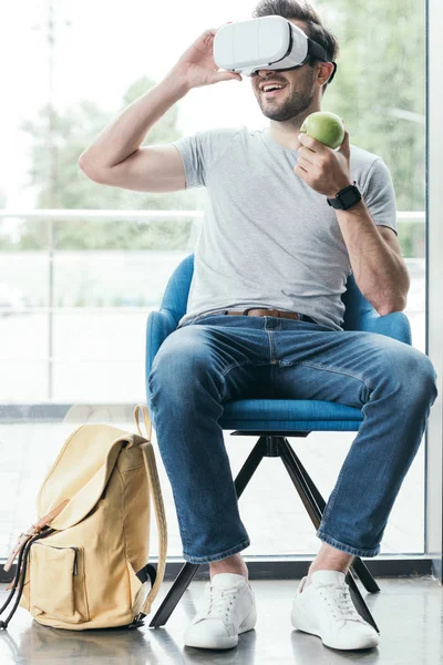 Sonriente joven sosteniendo manzana y usando auriculares de realidad virtual - foto de stock