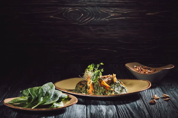 Plates with spinach leaves and panikesh near bowl with cashew nuts on wooden table — Stock Photo