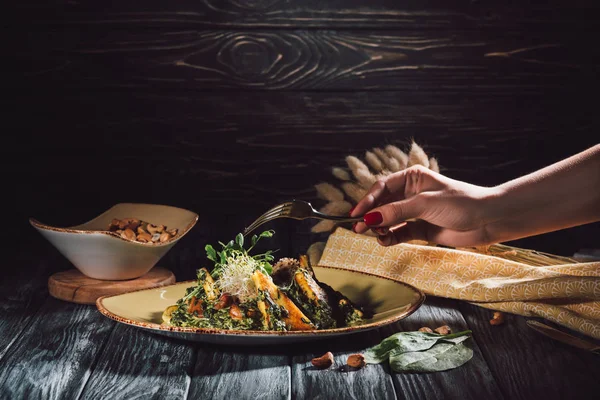 Imagen recortada de mujer comiendo panikesh con nueces de anacardo y espinacas por tenedor sobre la mesa - foto de stock