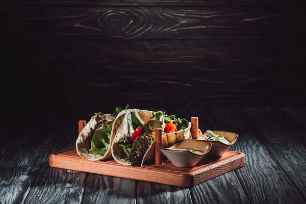 Tortilhas com falafel, tomate cereja e sementes germinadas de girassol em bandeja de madeira com molhos — Fotografia de Stock