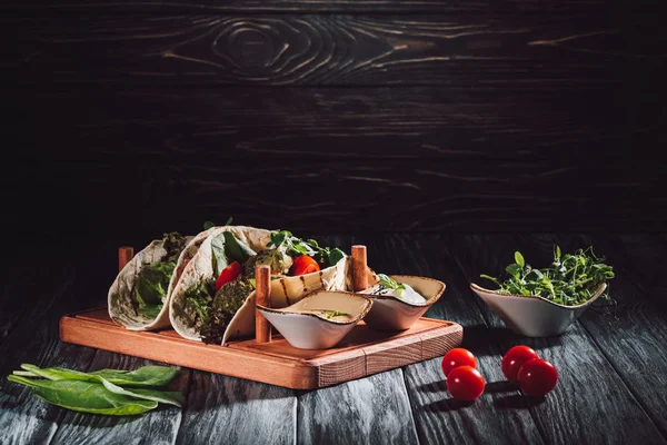 Food composition of tortillas with falafel, cherry tomatoes and germinated seeds of sunflower on wooden tray with sauces on table — Stock Photo