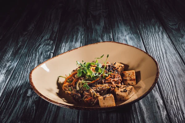 Primer plano vista de soba con tofu y verduras decoradas con semillas germinadas de girasol en plato sobre mesa de madera - foto de stock