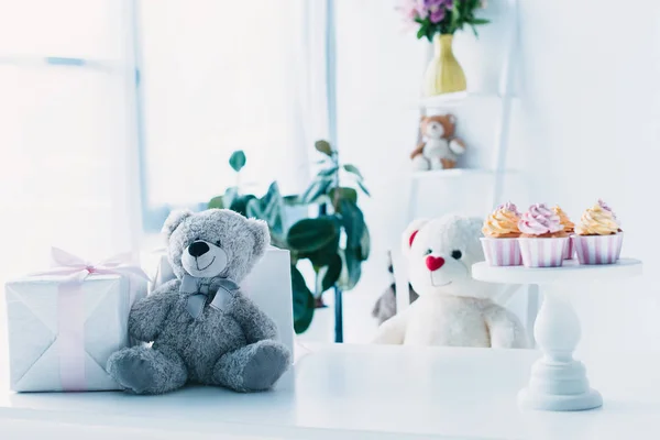 Ursinhos de pelúcia na mesa com caixa de presente e cupcakes em stand — Fotografia de Stock