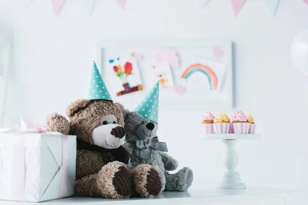 Ursinhos de pelúcia em cones na mesa com cupcakes no carrinho e caixa de presente — Fotografia de Stock