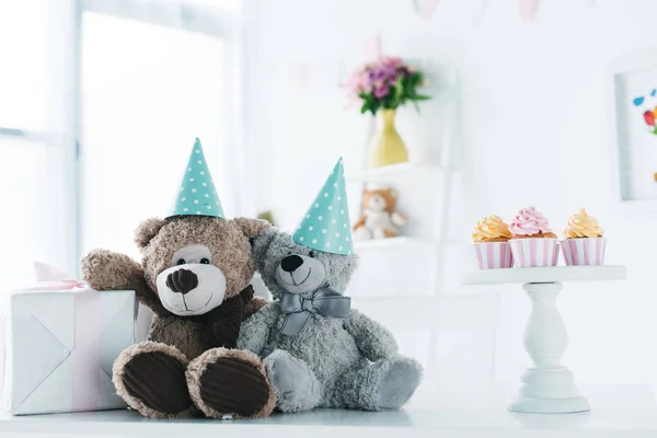 Osos de peluche en conos en la mesa con caja de regalo y cupcakes - foto de stock