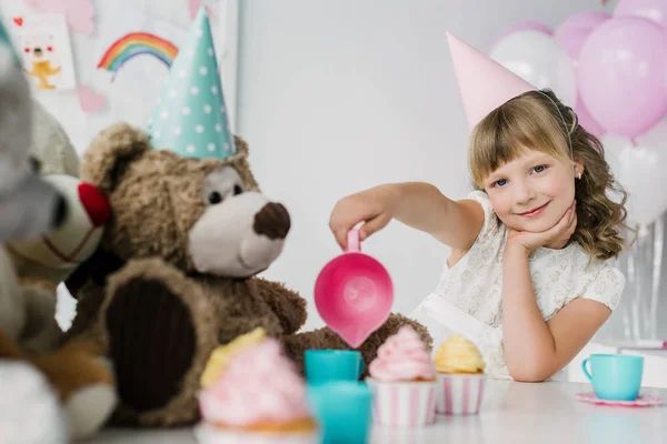 Niño de cumpleaños sonriente teniendo una fiesta de té con osos de peluche en conos - foto de stock