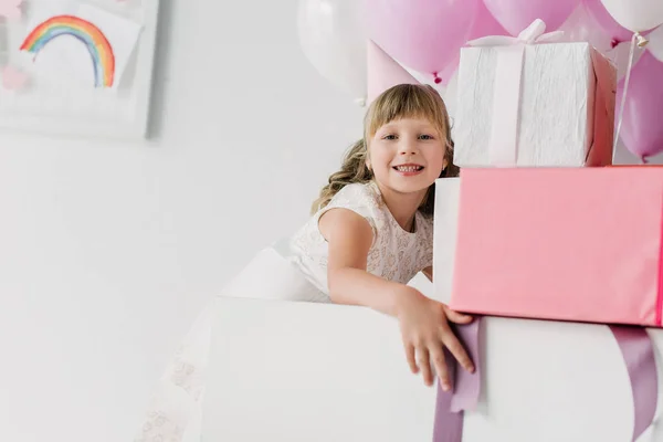 Feliz cumpleaños niño en cono mirando a la cámara y sosteniendo cajas de regalo - foto de stock