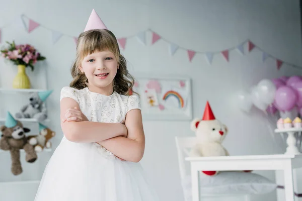 Smiling birthday girl in cone standing with crossed arms and looking at camera — Stock Photo