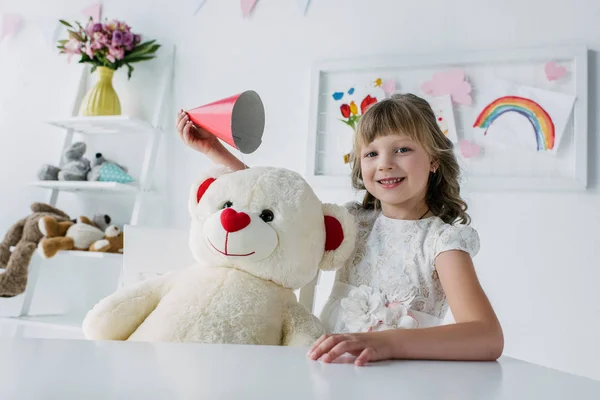 Glückliches Geburtstagskind mit Kegel über Teddybär — Stockfoto