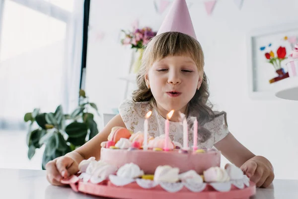 Happy adorable kid in cone blowing out candles from birthday cake — Stock Photo