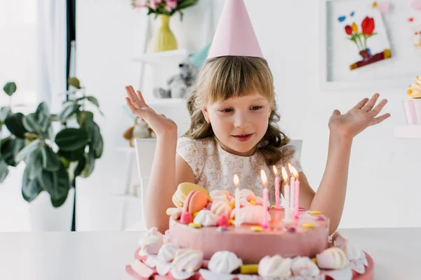 Cute kid with wide arms looking at birthday cake with candles — Stock Photo