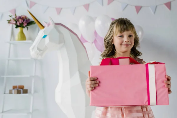 Niño feliz cumpleaños sosteniendo caja de regalo cerca de unicornio decorativo - foto de stock