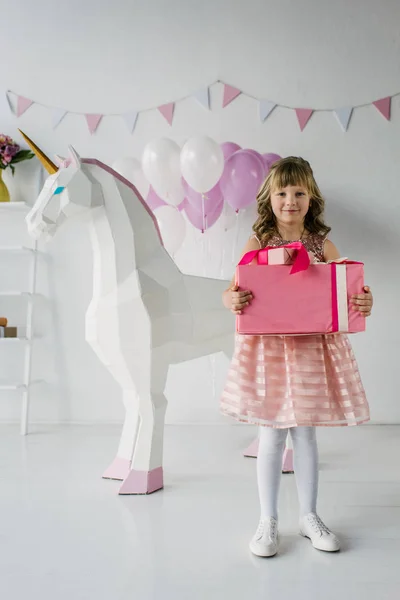Cute birthday child holding gift box near decorative unicorn — Stock Photo