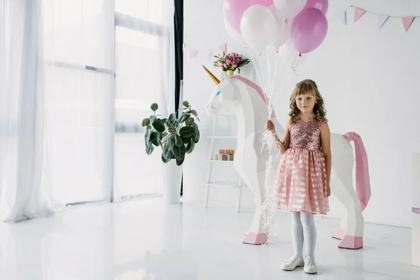 Bambino di compleanno che tiene mazzo di palloncini d'aria e in piedi con unicorno decorativo — Foto stock