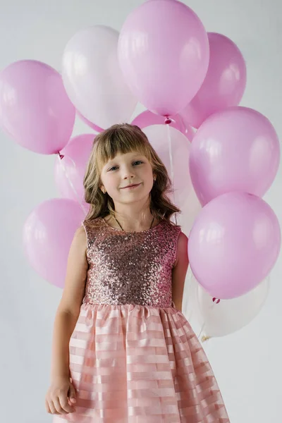 Lächelndes kleines Kind, das in die Kamera schaut und Luftballons in der Hand hält — Stockfoto