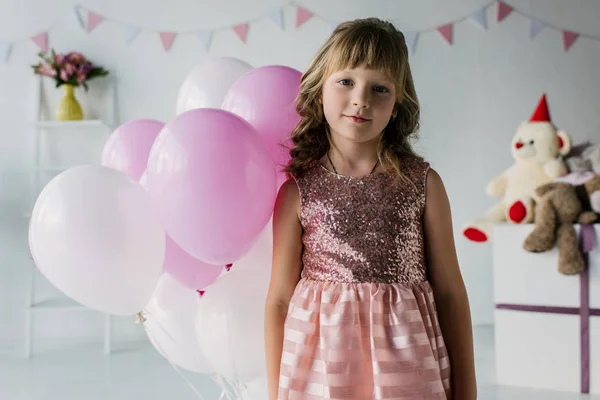 Entzückendes kleines Kind blickt in die Kamera und steht mit Luftballons — Stockfoto