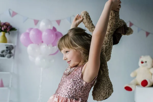 Vista lateral del niño sonriente sosteniendo un osito de peluche - foto de stock