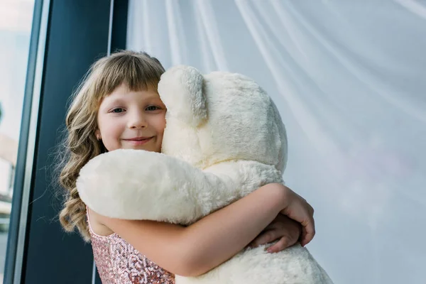 Porträt eines glücklichen Kindes, das in die Kamera blickt und einen weißen Teddybär umarmt — Stockfoto