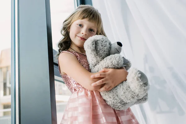 Criança feliz olhando para a câmera e abraçando ursinho de pelúcia — Fotografia de Stock