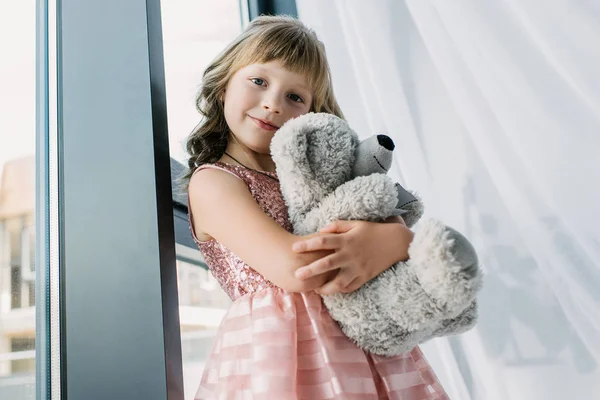 Heureux petit enfant regardant caméra et embrasser ours en peluche — Photo de stock