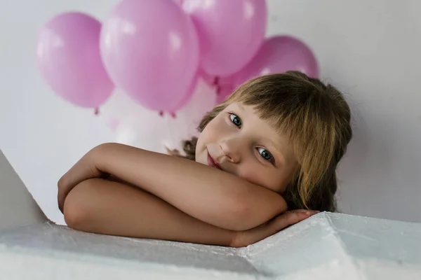 Ritratto del bambino sorridente che guarda la macchina fotografica con i palloncini rosa dietro — Foto stock