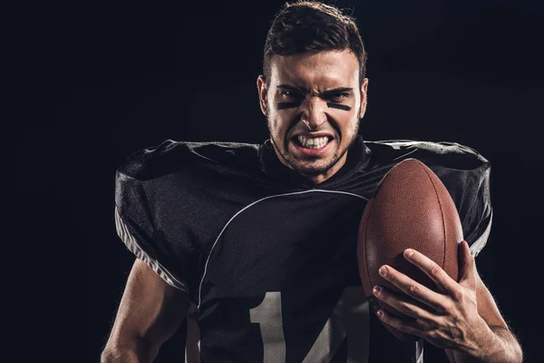 Ritratto ravvicinato di giocatore di football americano arrabbiato con palla guardando la fotocamera isolata sul nero — Foto stock