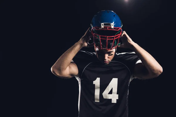 Joven jugador de fútbol americano que se pone el casco aislado en negro - foto de stock