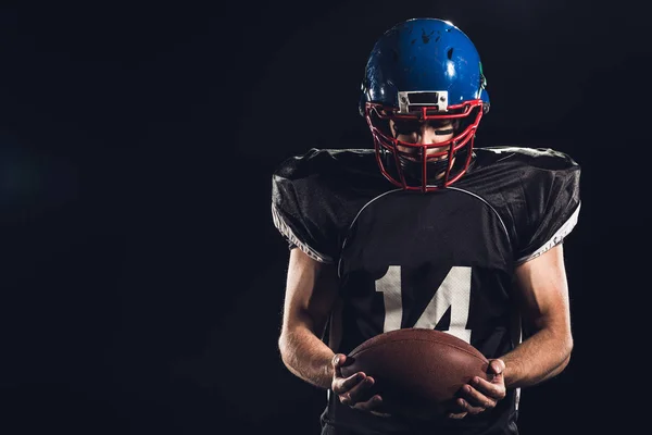 Американський футбол player дивлячись на м'яч у руки, ізольовані на чорному — стокове фото