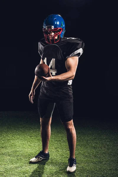 Handsome american football player with ball looking at camera on black — Stock Photo