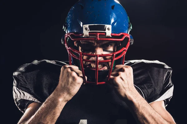 Nahaufnahme Porträt eines wütenden amerikanischen Fußballspielers mit Helm, der isoliert auf schwarz in die Kamera blickt — Stockfoto