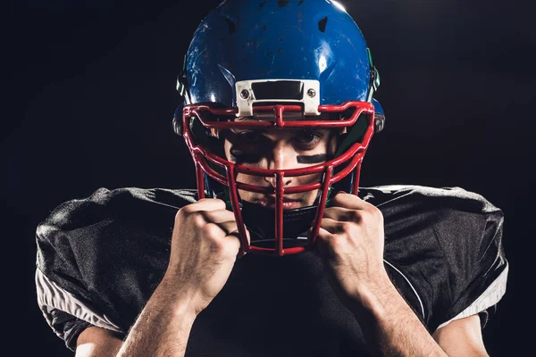 Retrato de primer plano del jugador de fútbol americano en casco mirando a la cámara aislada en negro - foto de stock