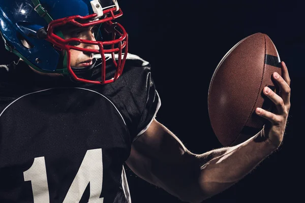 Close-up portrait of equipped american football player with ball isolated on black — Stock Photo