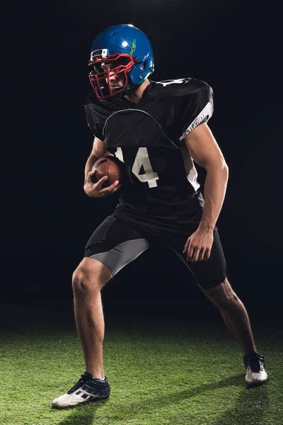 Joueur de football américain avec ballon sur herbe verte sur noir — Photo de stock