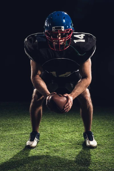 American Football-Spieler steht mit Ball auf dem Rasen und schaut in die Kamera auf schwarz — Stockfoto