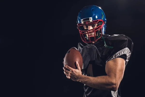 Jogador de futebol americano com bola olhando para câmera isolada em preto — Fotografia de Stock