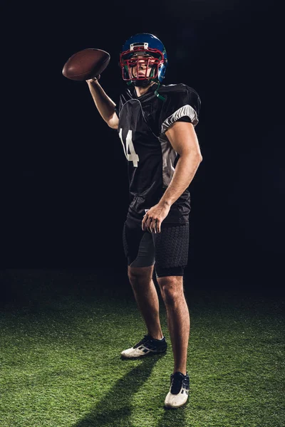 American football player on green grass throwing ball on black — Stock Photo